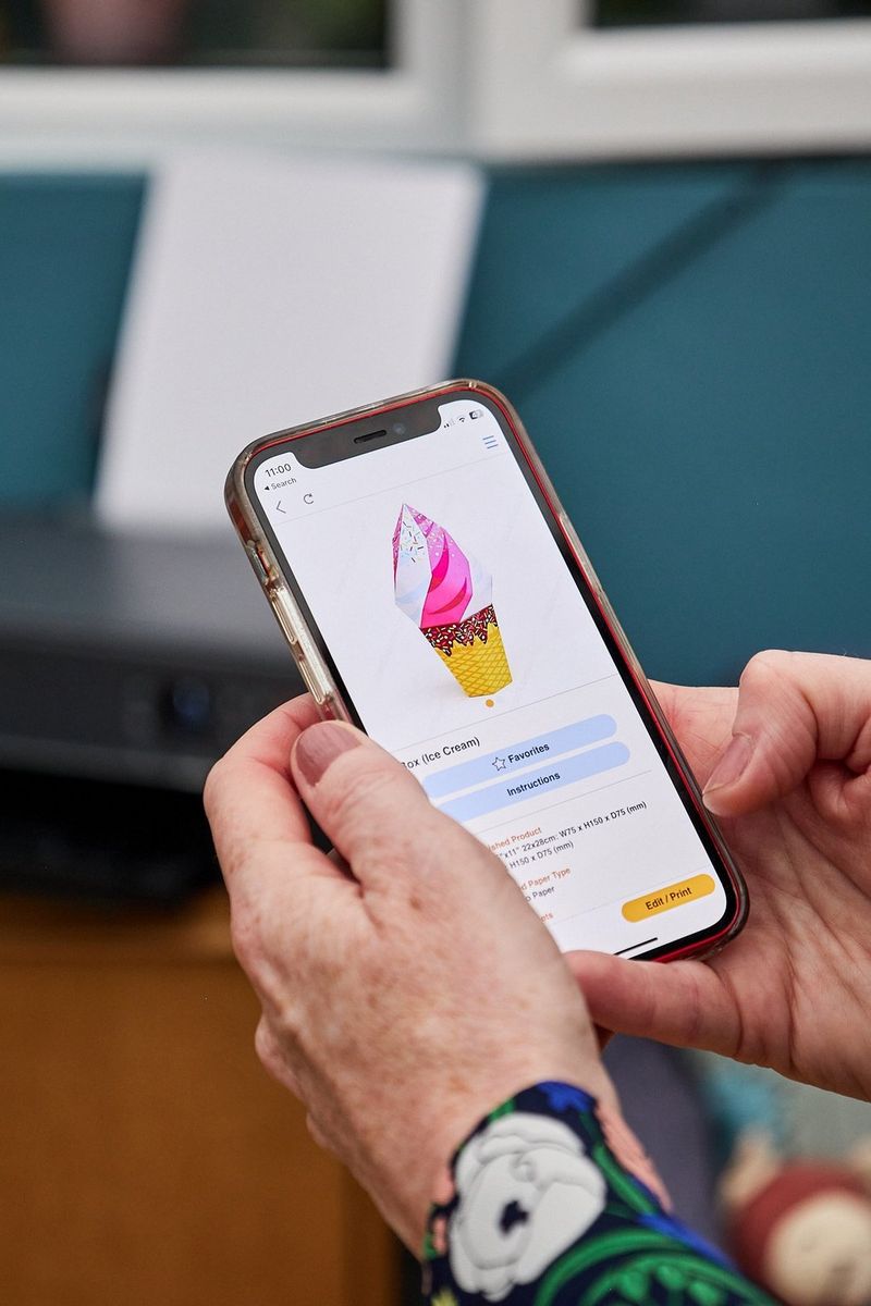 Ruce drží chytrý telefon, na kterém je v aplikaci Creative Park zobrazena zmrzlina z papíru.