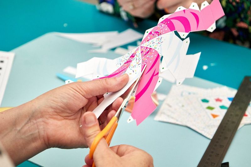 Ruce drží nůžky a stříhají jimi šablonu zmrzliny ze služby Creative Park.