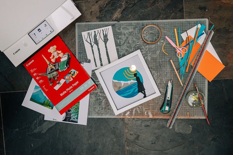 Una stampante Canon PIXMA su un pavimento in pietra con un tappetino da taglio e un assortimento di carta, il tutto fermo.