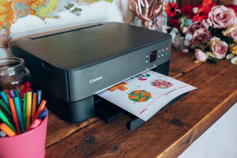 Een Creative Park-sjabloon rolt uit een zwarte Canon-printer die op een houten plank staat.