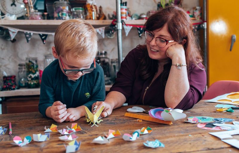Een glimlachende vrouw en een jongen zitten aan een tafel en spelen met fidget toys.