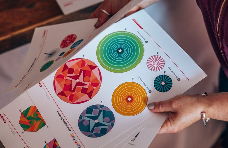 Handen houden een stapeltje kleurrijke Creative Park-sjablonen vast die zijn geprint op Canon Matglans Foto Papier.