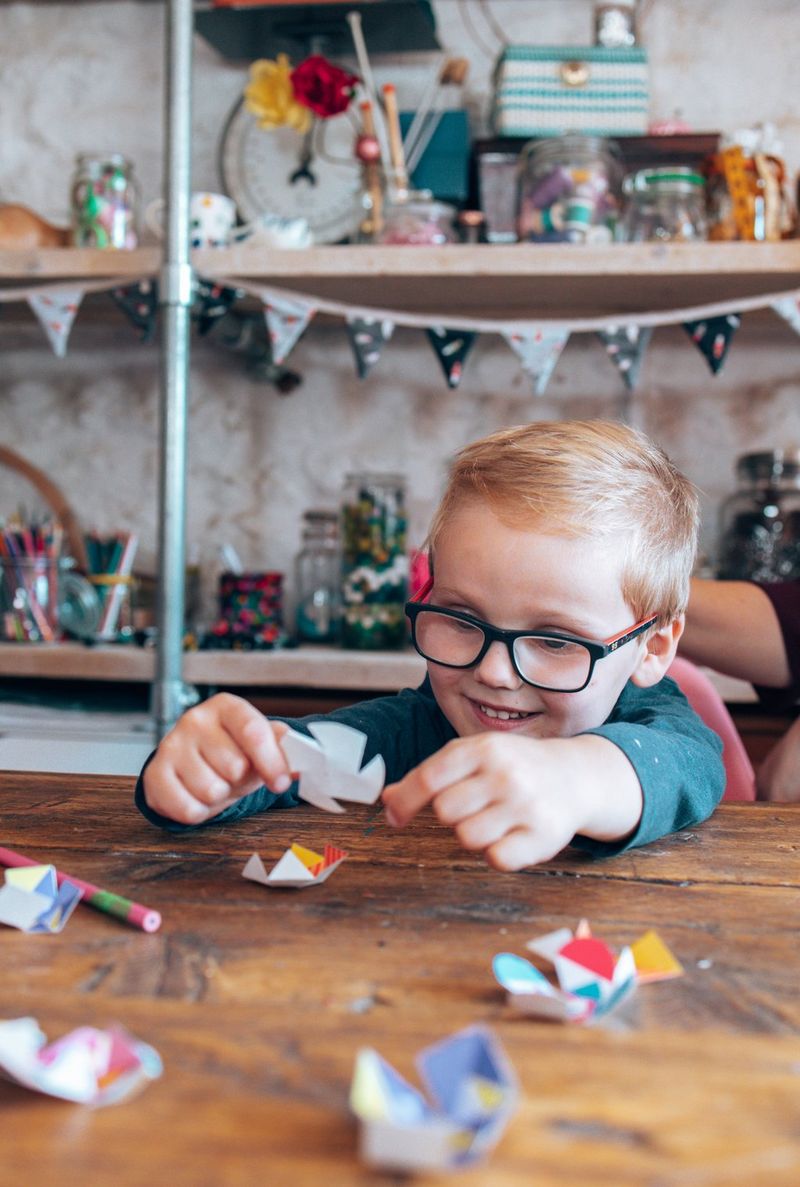 Een glimlachende jongen zit aan een tafel en speelt met papieren fidget toys.