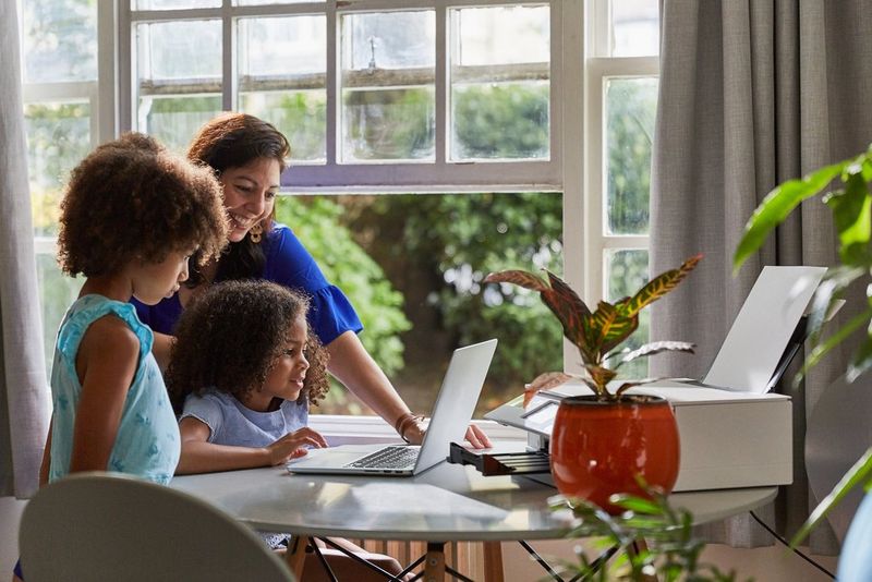 Мама с двумя детьми собрались за стеклянным столом возле ноутбука.
