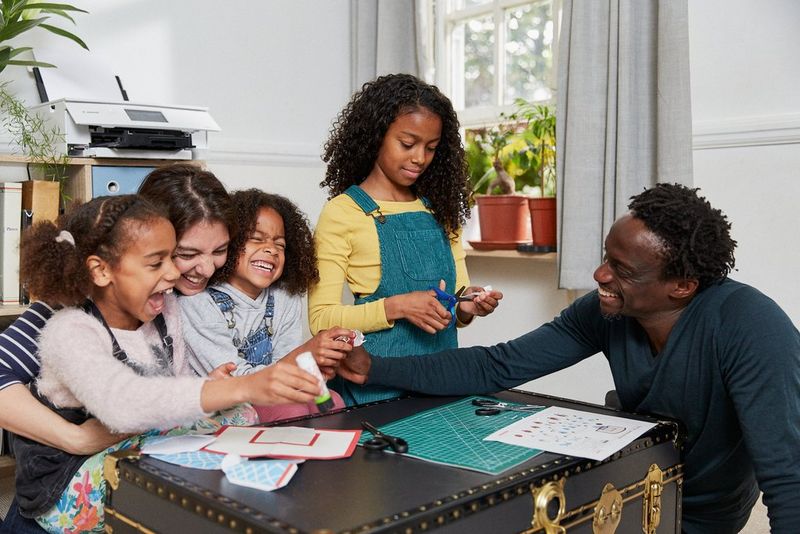 Družinski člani skupaj izrezujejo oblike in ustvarjajo izdelke iz papirja.