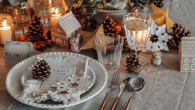 Detailní záběr jídelního stolu pokrytého lněným ubrusem a zdobeného borovými šiškami, listovím a předměty z papíru.