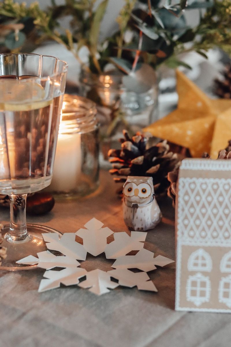 Detailní záběr stolu ozdobeného borovými šiškami, svíčkami a papírovými sněhovými vločkami, hvězdami, sovičkami a perníkovými chaloupkami vytvořenými pomocí aplikace Creative Park.