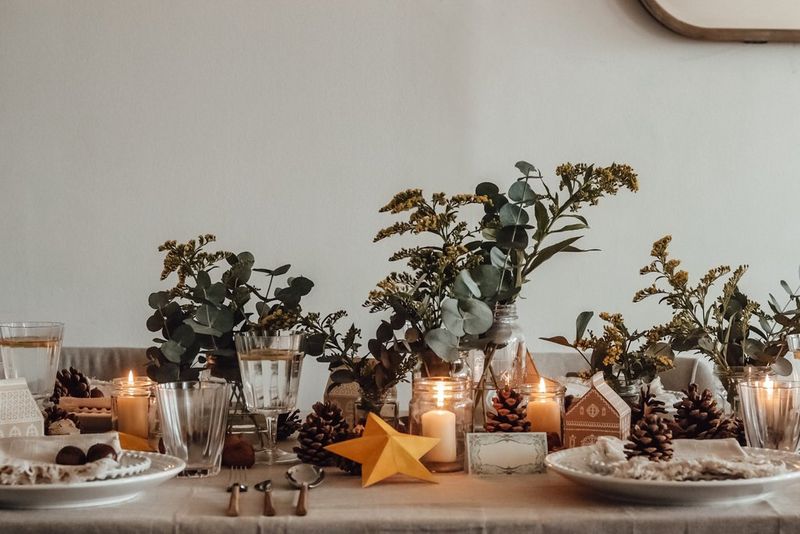 Krásně zdobený jídelní stůl pokrytý lněným ubrusem a ozdobený borovými šiškami, listovím a předměty z papíru.