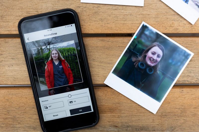 Pametni telefon s aplikacijom SELPHY Photo Layout i otisnuta portretna fotografija položeni na drveni stol, snimljeni odozgo.