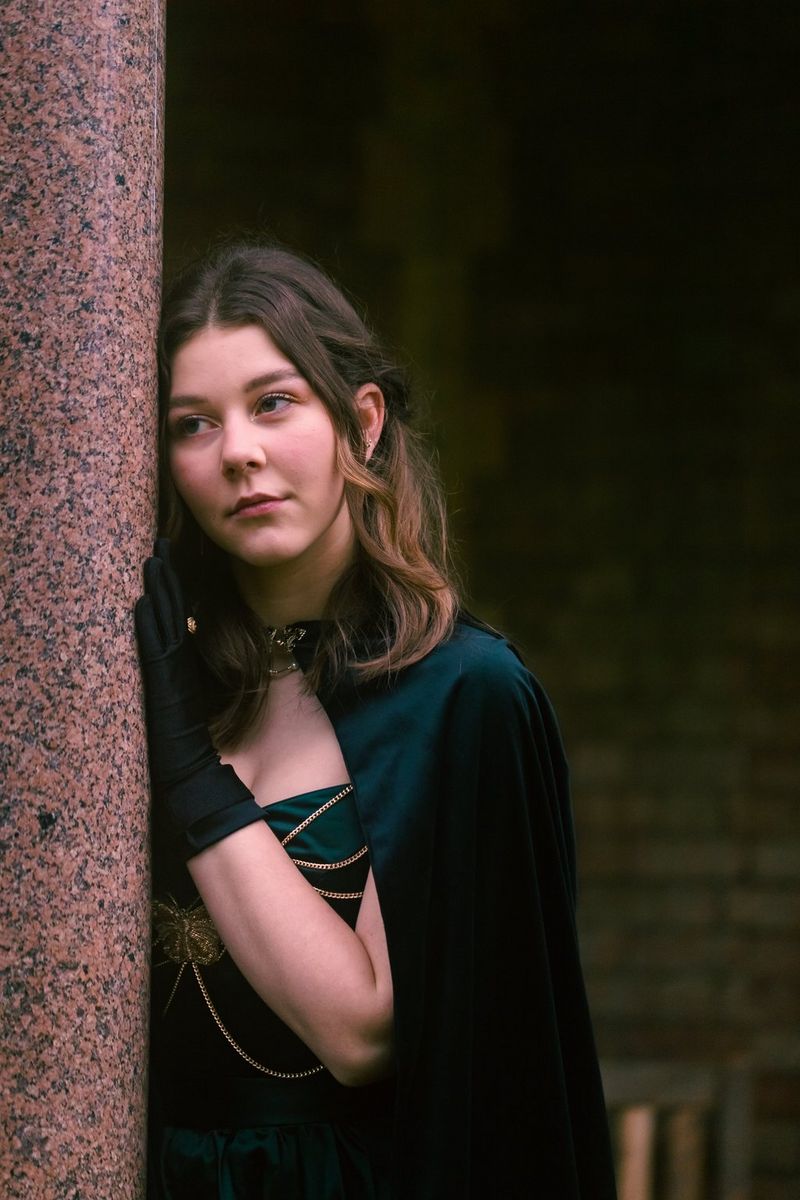 Oseba, oblečena kot princesa, sloni na zidu in hrepeneče pogleduje proti renesančnemu sejmu.