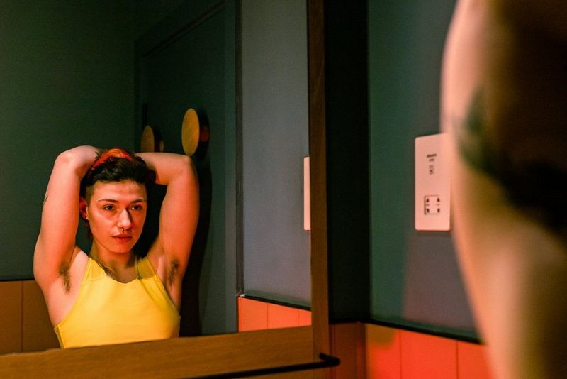 Na fotografiji Louis Painter trans glasbenik_ica Jay Page gleda v ogledalo z rokama sklenjenima za glavo.