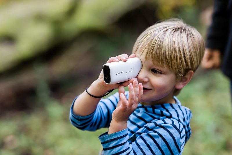 Un ragazzino guarda nel mirino di una fotocamera Canon PowerShot ZOOM.