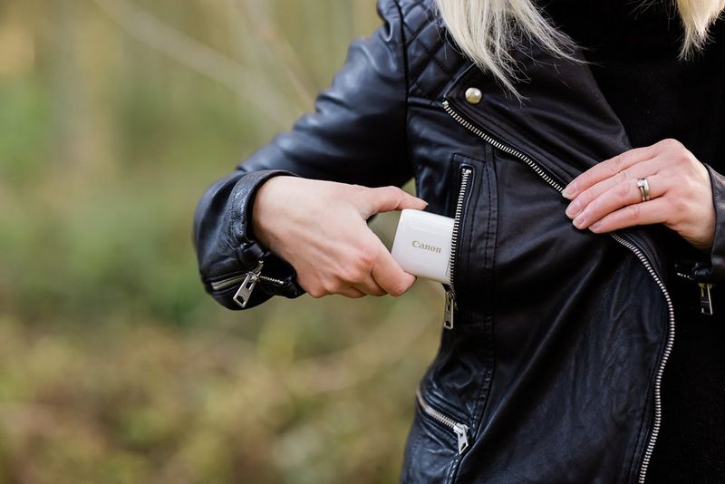 Una donna mette una fotocamera PowerShot ZOOM nella tasca della sua giacca di pelle.