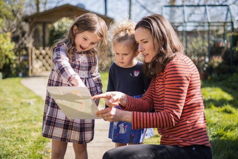 In een grote tuin kijkt een moeder samen met haar jonge dochters naar een schatkaart.