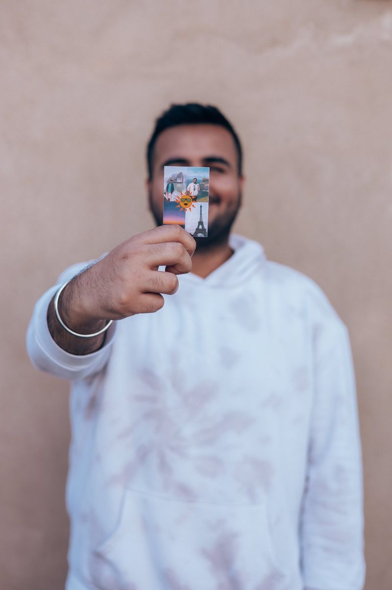 A man smiles at the camera, holding up a small print of holiday photos in front of his face.