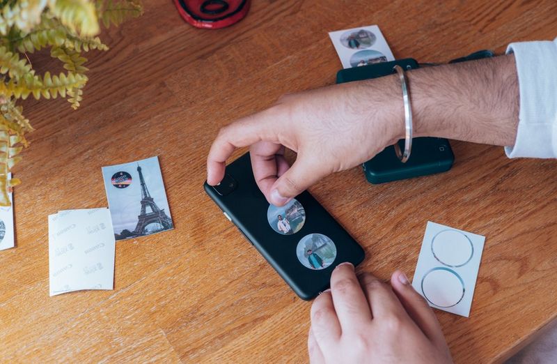 Hands place circular stickers on the back of a smartphone.
