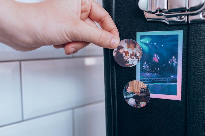 A black banjo case rests against a white tiled wall, with a person sticking Canon circle stickers onto it.