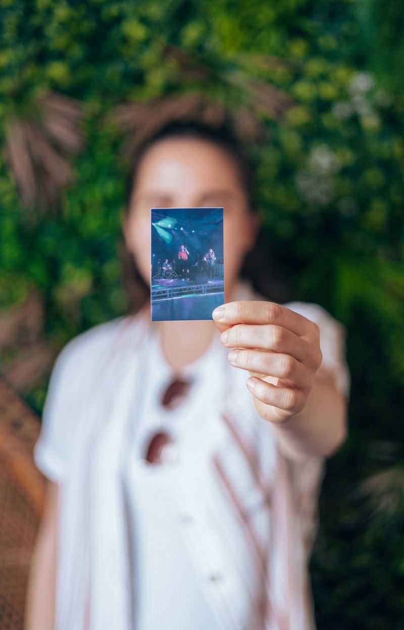 A woman looks straight towards the camera, holding a small print of herself on stage in front of her face.