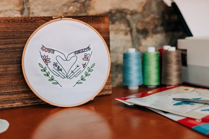 Кусок ткани в рамке с напечатанной схемой для вышивки в виде рук, сложенных в форме сердца.