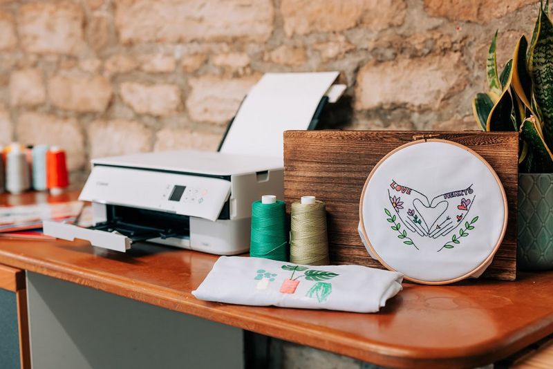 Футболка с напечатанной вышивкой и настенное панно рядом с принтером Canon.
