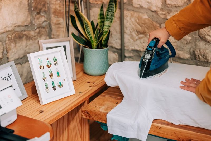 Женщина проглаживает футболку утюгом, узор для термопереноса расположен лицевой стороной вниз.