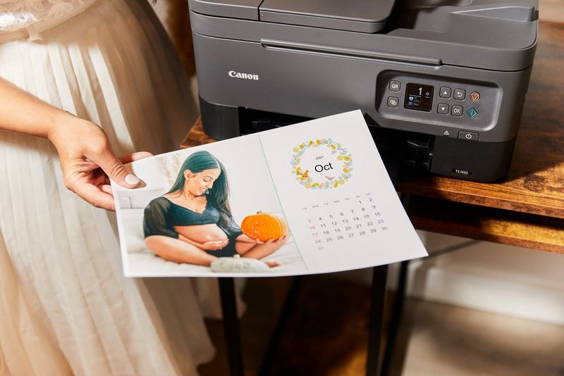 אישה מחזיקה דף של לוח שנה לחודש אוקטובר בו נראית אישה בהריון מחזיקה דלעת ליד הבטן שלה.