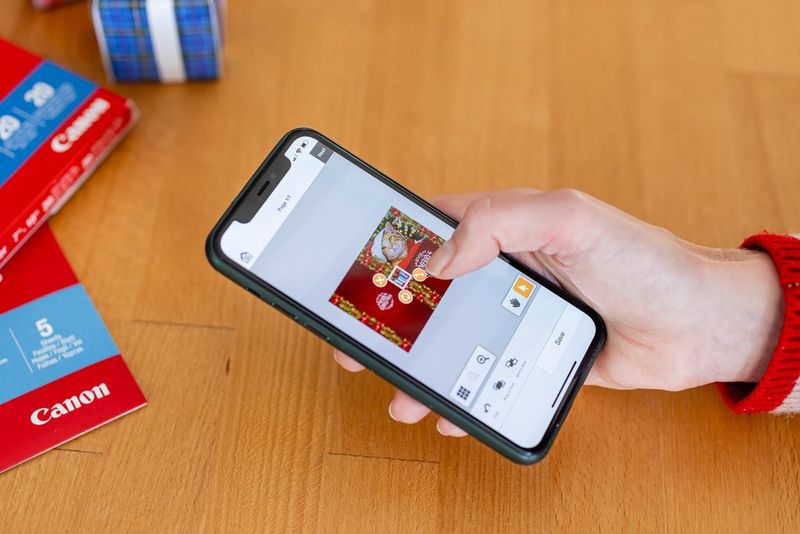 Iemand die een smartphone gebruikt om zijn/haar kerstkaartontwerp te bewerken in de Easy-PhotoPrint Editor-app.
