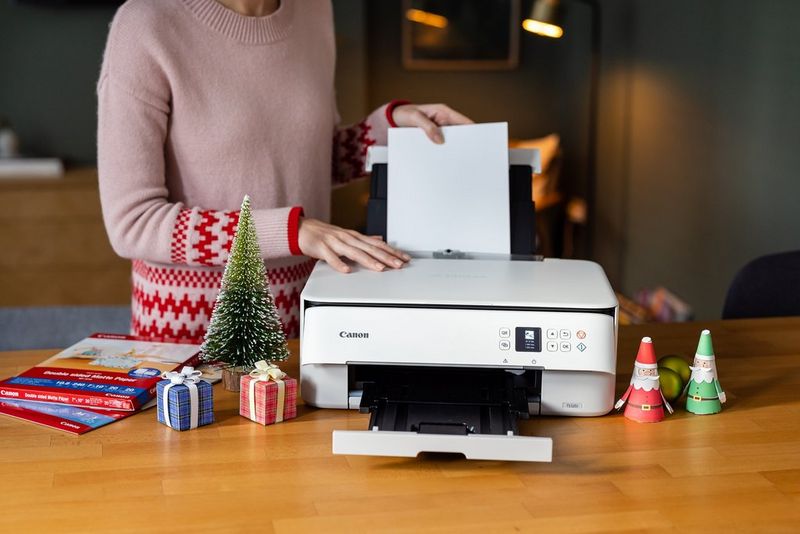 Een vrouw in een kersttrui die papier plaatst in een Canon PIXMA-printer.