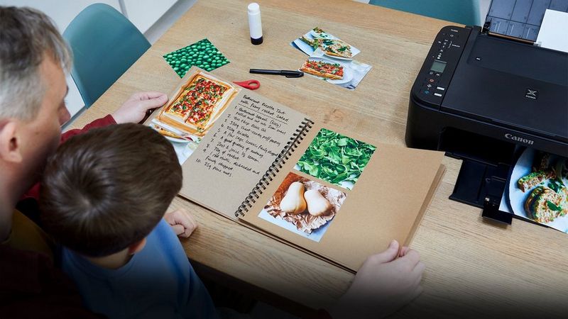 A father and son flick through the pages of a recipe book together.