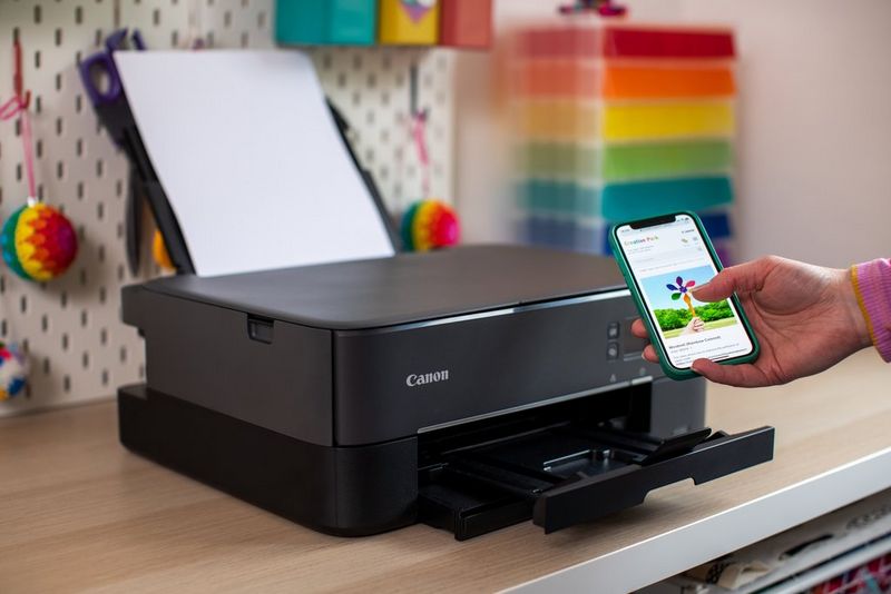 Een hand houdt een smartphone vast met op het scherm een windmolensjabloon van Canon Creative Park. Op de achtergrond staat op een bureau een Canon PIXMA-printer.