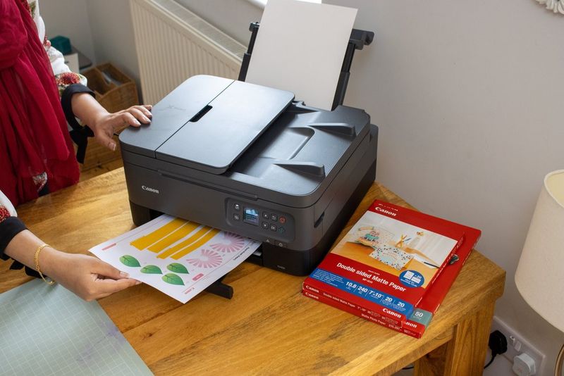 Une imprimante, posée sur une table à côté de papier pour imprimante Canon, imprime une feuille de motifs Creative Park.