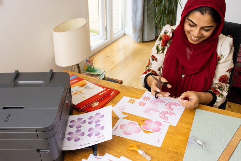 Une femme souriante, en train de découper des fleurs avec des ciseaux.