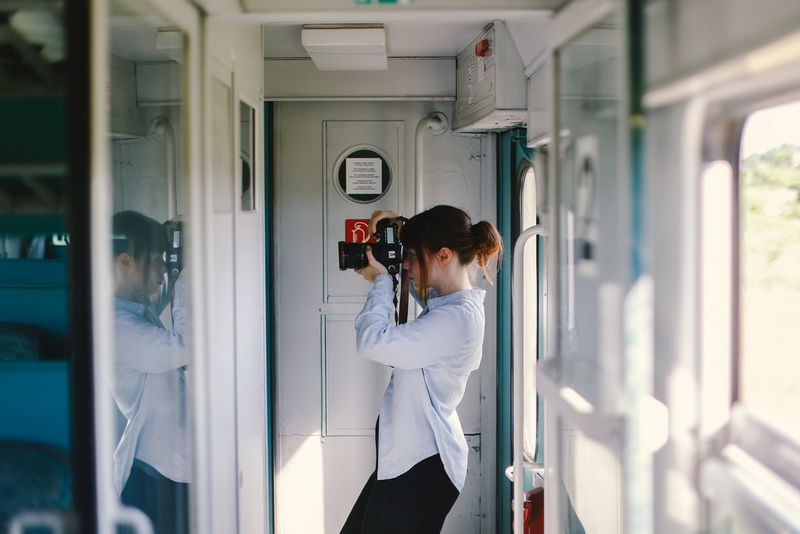 Travel photographer Katie Edwards stands in the vestibule of a train, taking photos out of the window with a Canon camera.