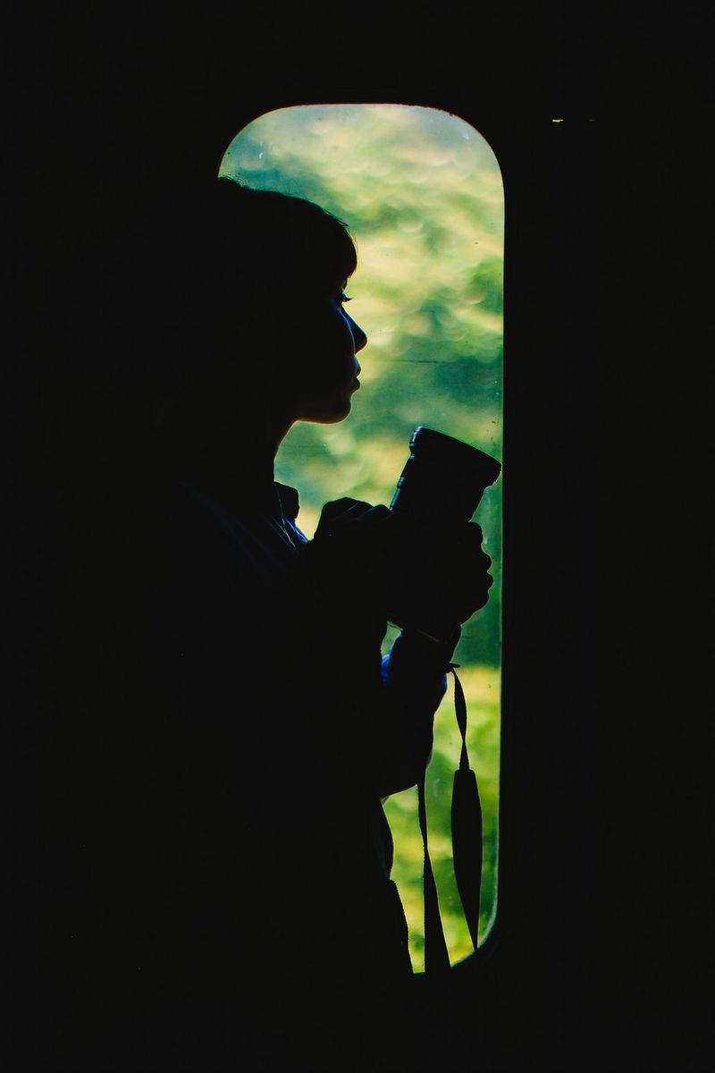 Travel photographer Katie Edwards stands silhouetted in the window of a train door, holding her Canon camera.