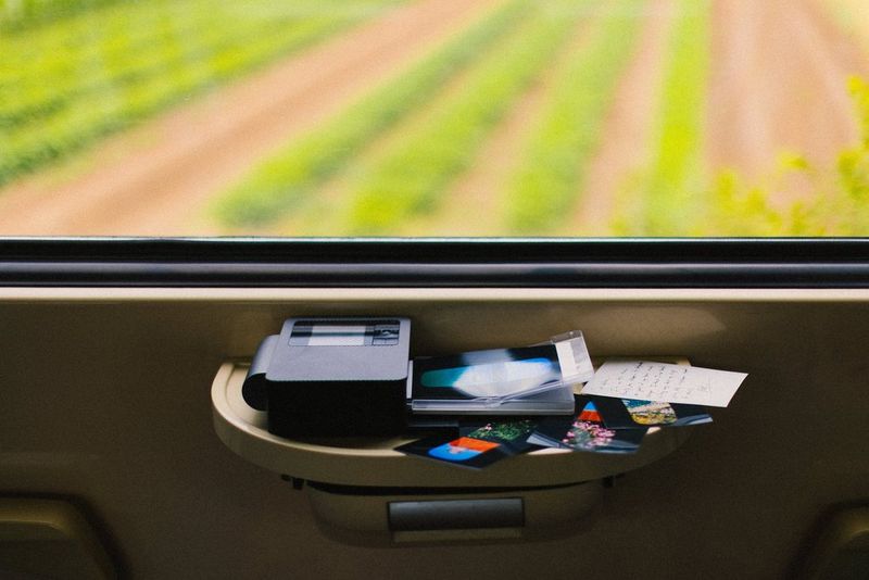 A Canon SELPHY CP1500 portable photo printer sits on the small table below a train window, with a photo print in its output tray and various other prints scattered around.