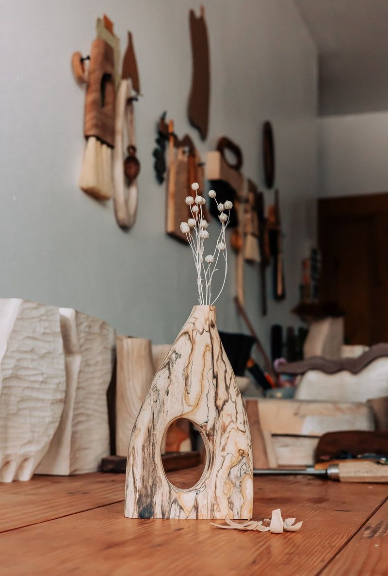 Vaso di legno pieno di piccoli fiori bianchi su un tavolo accanto a un cesello per legno.