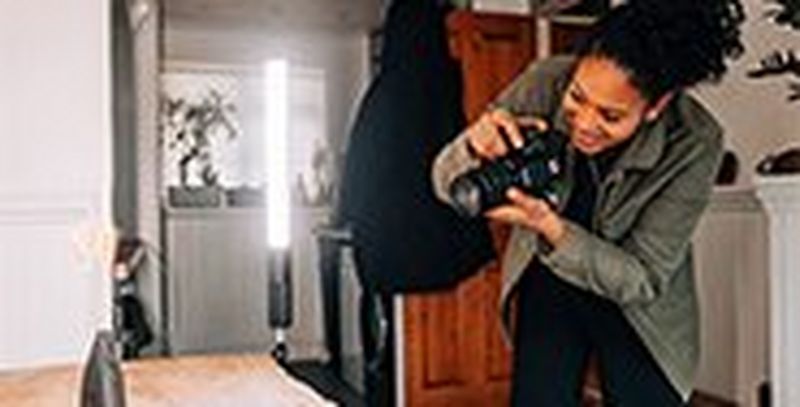 A woman using a EOS 850D to photograph a wooden vase on a table, lit by an LED light.