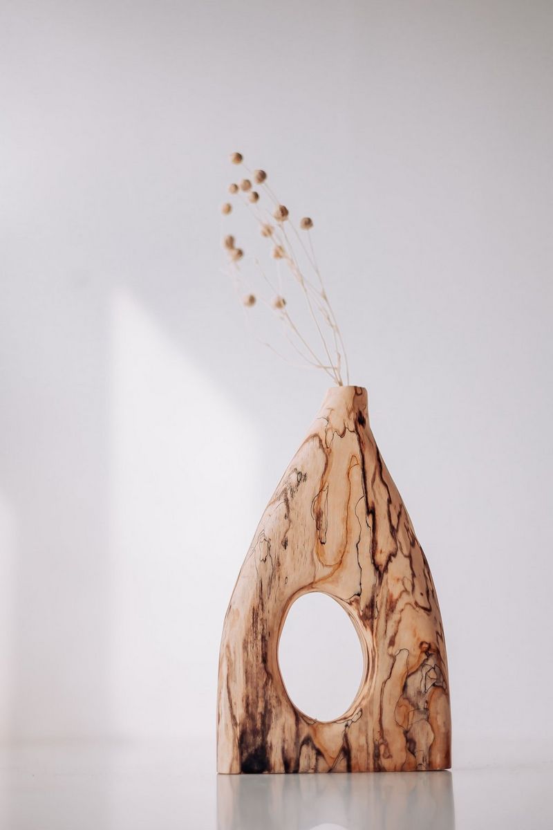 Vaso di legno riempito di fiori secchi su sfondo bianco con luce naturale.