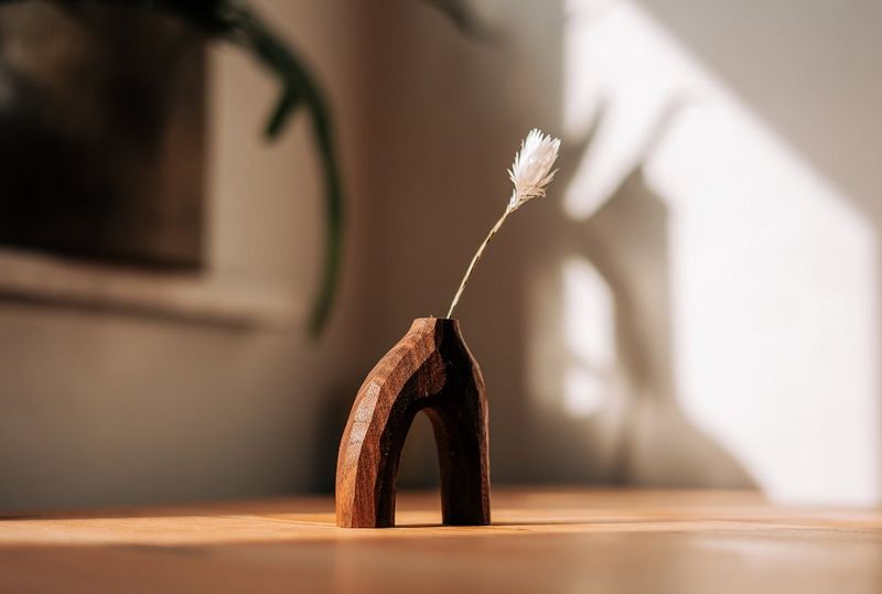 Vaso in legno intagliato con un po' di erba secca al suo interno, illuminato dalla luce solare proveniente da una finestra.