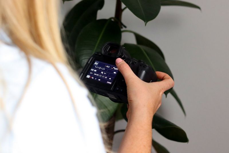 Roka drži fotoaparat z različnimi nastavitvami, vidnimi na zadnjem zaslonu.