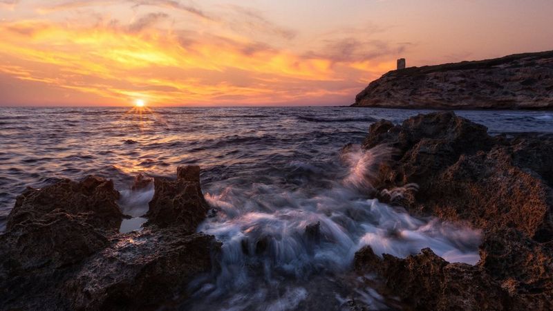 Сделанная Эриком Коломбо фотография HDR, на которой можно увидеть небо, линию горизонта и беспокойные морские волны, разбивающиеся о скалы на переднем плане, — все это на фоне теплых оттенков вечернего неба.