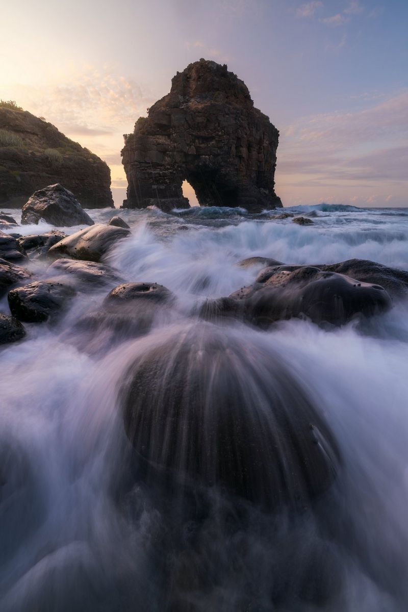 Сделанная Эриком Коломбо фотография скалистого побережья, природной формации в виде арки и размытых благодаря длительной выдержке воронок морской воды, проходящей через камни на переднем плане.