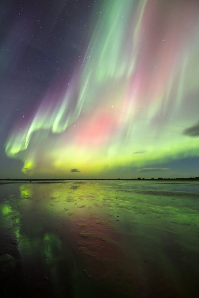 На этой фотографии, сделанной Эриком Коломбо, в небе можно увидеть северное сияние, краски которого отражаются в ледяном море. Темная линия на горизонте — это суша.