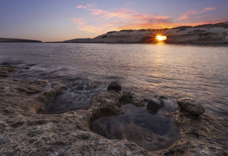 Составная фотография HDR, сделанная Эриком Коломбо, на которой через естественную формацию в форме арки запечатлено заходящее солнце. На переднем плане морские волны накатывают на скалистый берег.