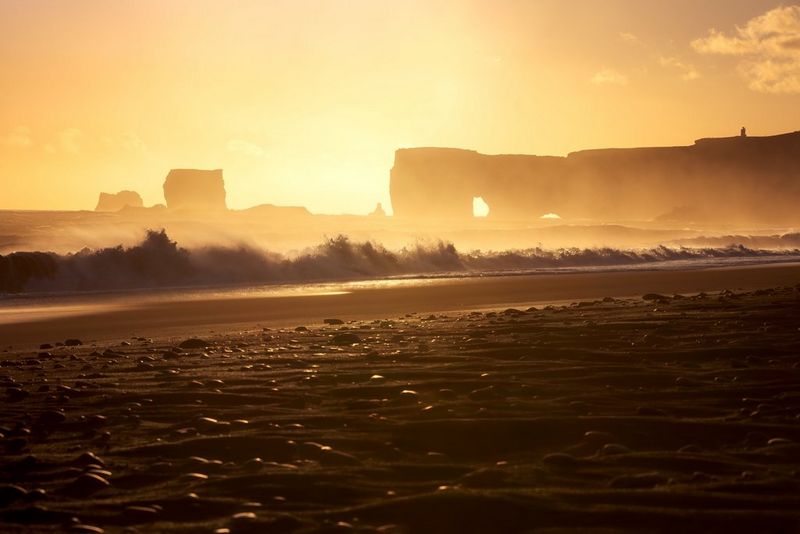 Сделанная Эриком Коломбо фотография, на которой волны разбиваются о берег и словно застывают в движении, а на фоне можно увидеть окутанные дымкой и теплым предзакатным сиянием скалистые формации.