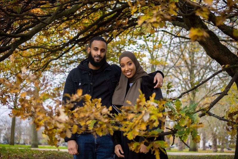 Un cuplu într-un peisaj împădurit, înconjuraţi de frunzele tomnatice ale arborilor.