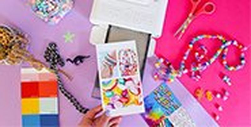 A hand taking a printed sheet of vibrant images from a Canon SELPHY CP1300 printer surrounded by beads, necklaces and a colour chart.
