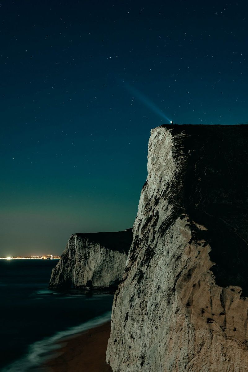 Звезды светят в ночном небе над скалами и пляжем.