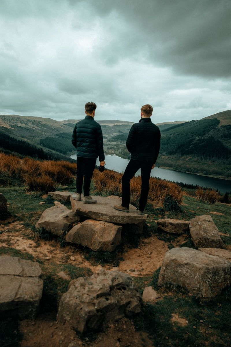Двое мужчин стоят на камне перед долиной, где течет река.