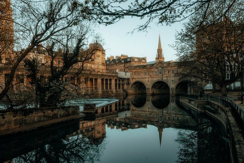 Мост Палтни отражается от гладкой поверхности реки, которую он пересекает.